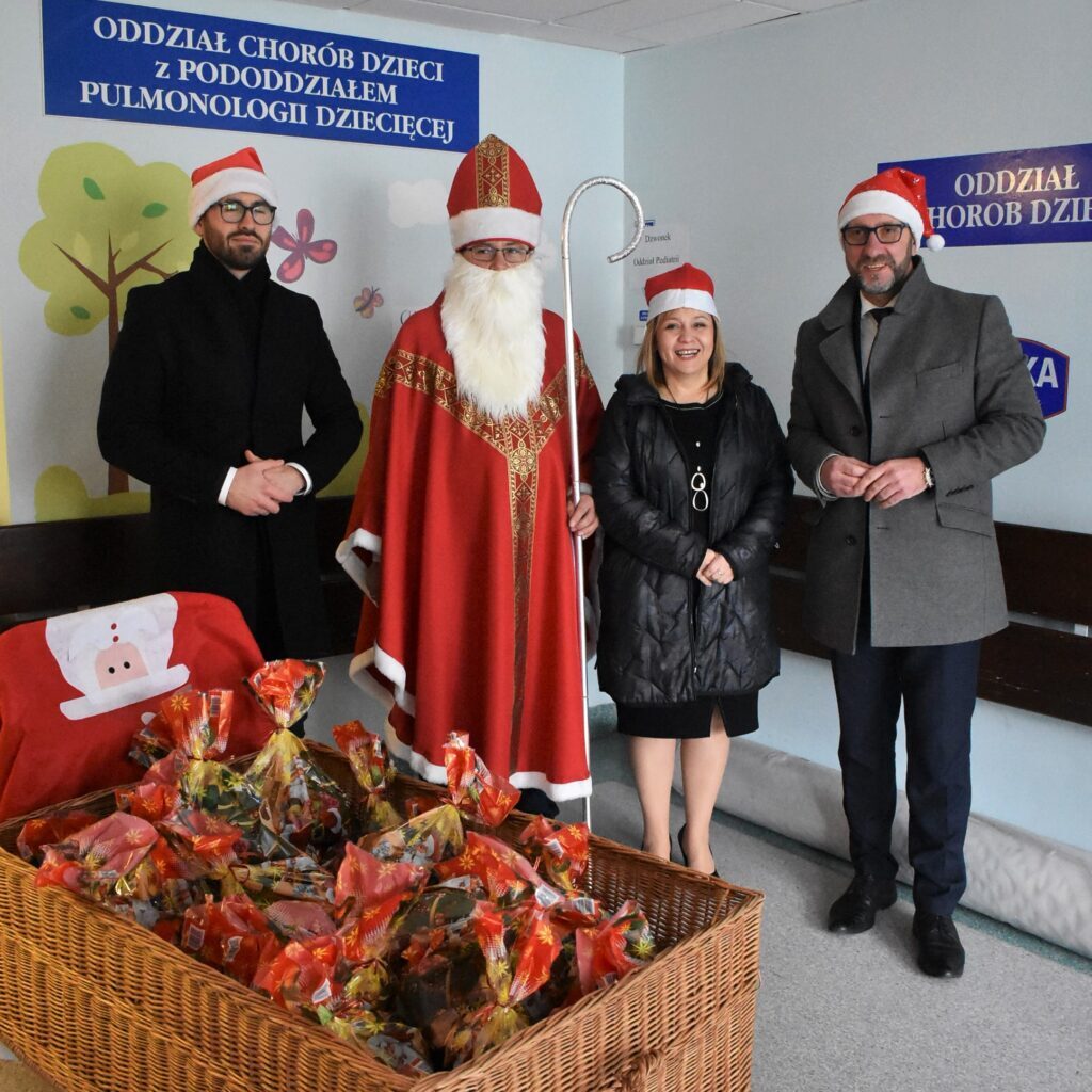 Mikołaj z dyrektor szpitala oraz wiceprezydentem i kierownikiem biura prezydenta, przed nimi stoi kosz z prezentami