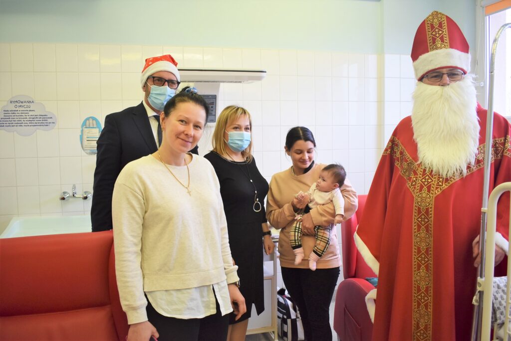 Mikołaj z dyrektor szpitala i wiceprezydentem oraz dziecko na rękach mamy, obok jego babcia