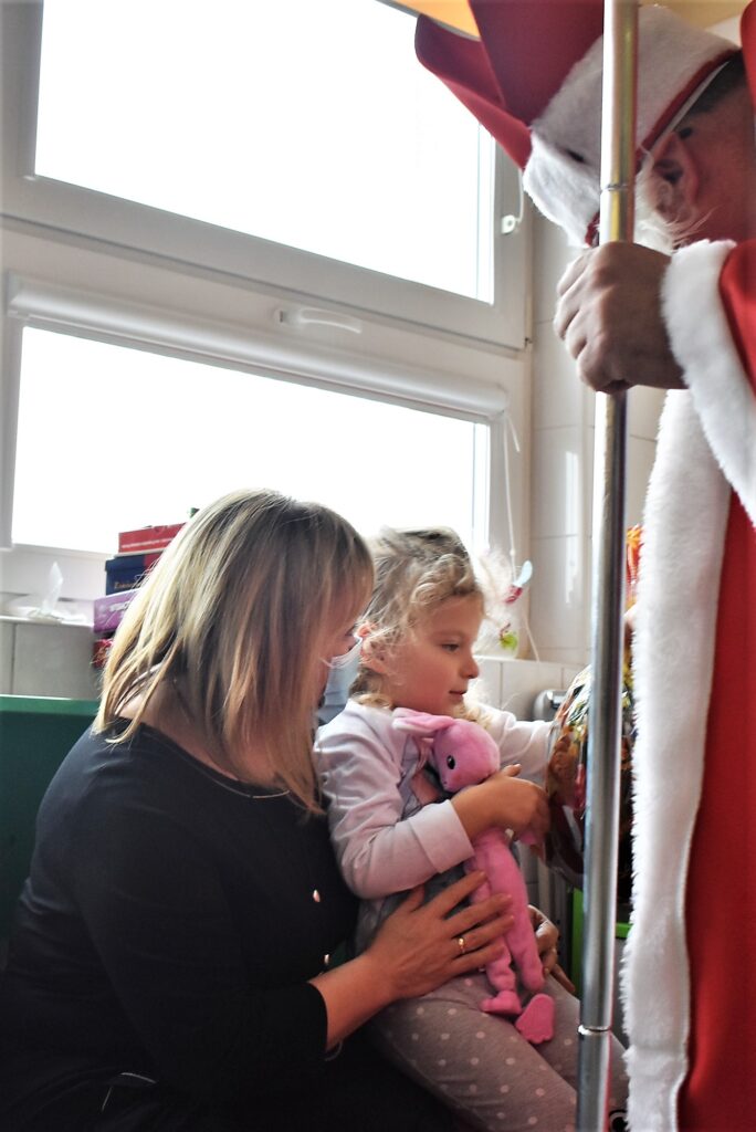 Dziecko siedzi na kolanach u dyrektor szpitala, Mikołaj wręcza mu prezent